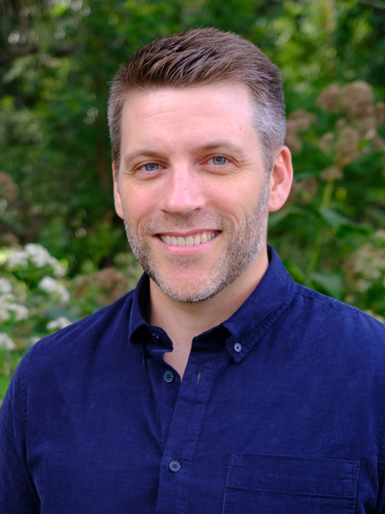 Headshot of Nathan Jandl wearing a blue shirt in front of a green background