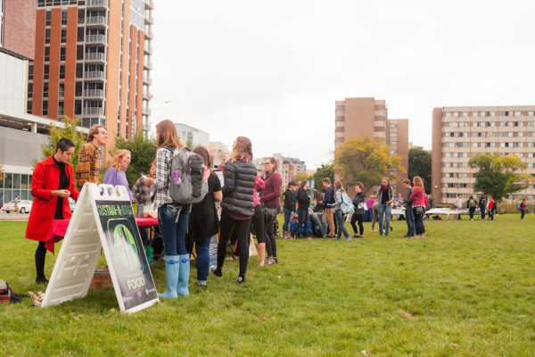 Students stand on a grassy lawn with tall buildings in the background