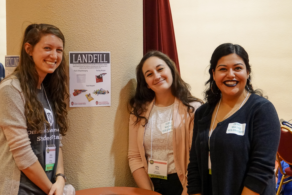 Intern volunteers Anna Weinberg, Ally Burg, and Noemy Serrano (L-R) pose near a zero waste station in the exhibitor hall at Monona Terrace.