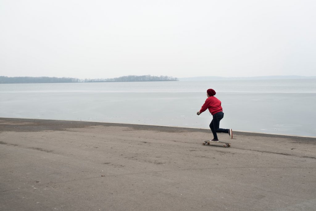 While many Badgers have left campus for winter break, a lone woman rolls her longboard along the Memorial Union Terrace at the University of Wisconsin-Madison past a partially frozen Lake Mendota on Dec. 21, 2014. In the background is Picnic Point. (Photo by Jeff Miller/UW-Madison)