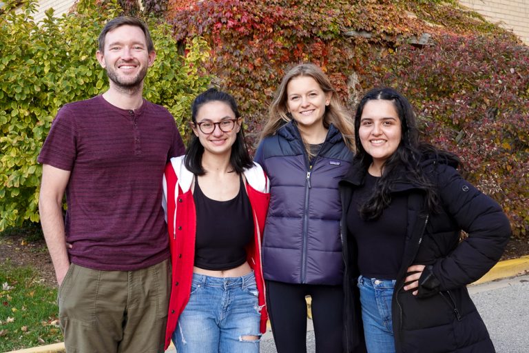 Four people smiling in front of red and green ivy