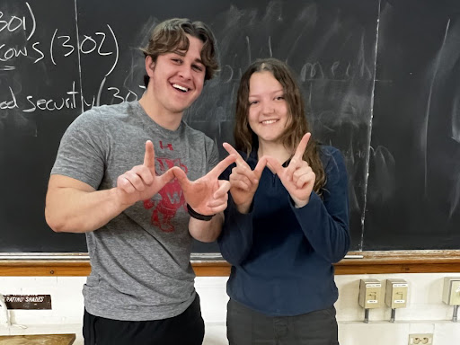 Caroline Crawley and Grady LaJeunesse stand in front of a chalkboard making a Wisconsin W sign with their fingers