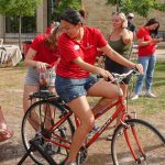 Young woman in red shirt pedals a red bike with a blender on the rear seat filled with fruit