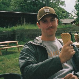 Young man with moustache and brown cap eating an ice cream cone