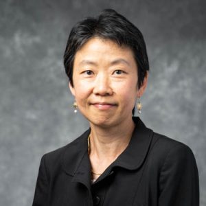 Woman with short black hair and a black blouse in front of a gray background