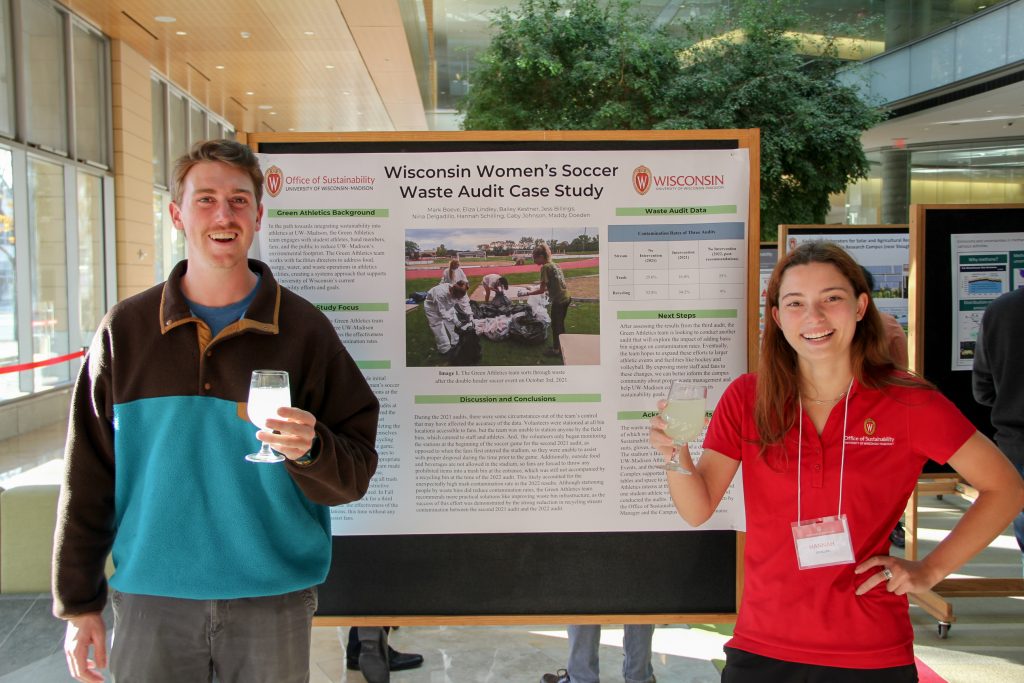 Two people standing and smiling in front of a poster presentation.