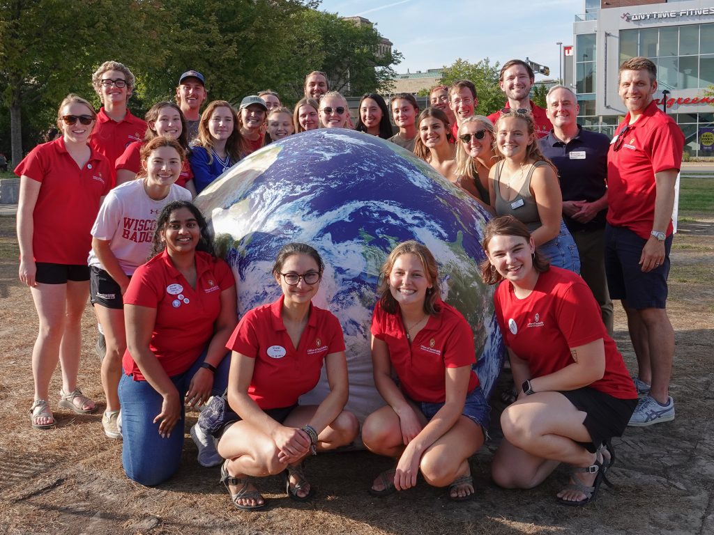A group of people in red shirts surrounding a large, inflated Earth.