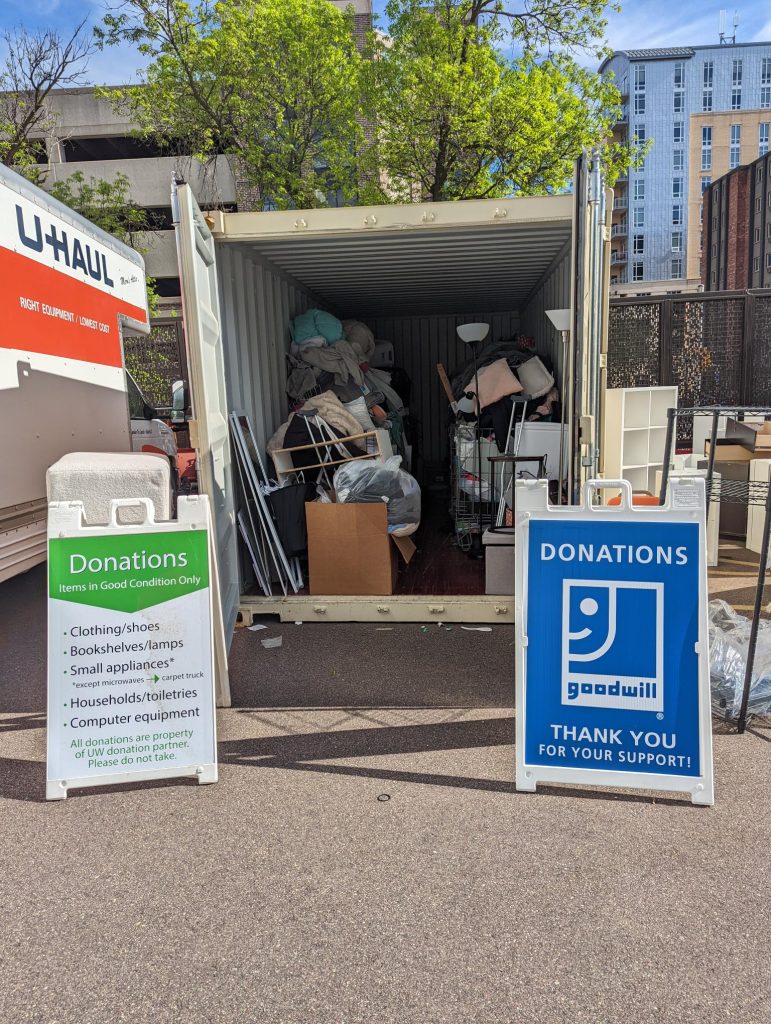 A move out truck welcomes residents with open doors and two signs showing donation informationn. 
